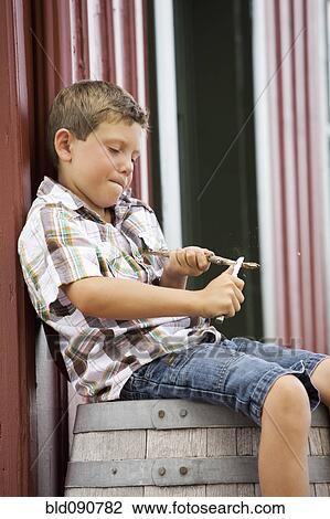 Stock Image - Caucasian boy sitting on barrel whittling stick. Fotosearch