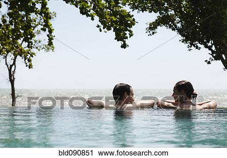 Stock Image - Caucasian couple swimming in infinity pool together. Fotosearch