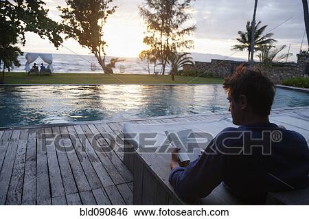 Stock Photograph - Caucasian man reading at poolside. Fotosearch