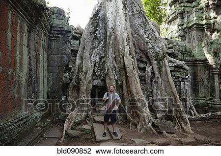 Stock Image - Caucasian man standing by large tree roots in ruins. Fotosearch