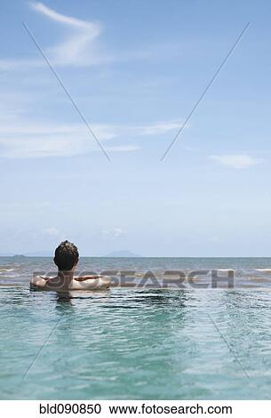 Stock Image - Caucasian man swimming in infinity pool. Fotosearch