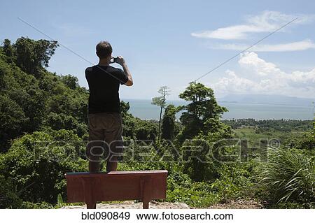 Stock Photo - Caucasian man taking photograph of remote area. Fotosearch