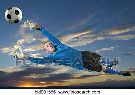 Stock Photograph - Caucasian soccer goalie jumping in mid-air catching ball. Fotosearch