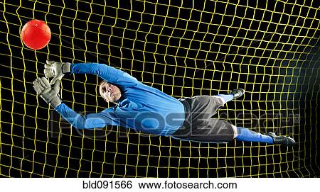 Stock Photograph - Caucasian soccer goalie jumping in mid-air catching ball at night. Fotosearch