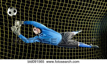 Stock Photography - Caucasian soccer goalie jumping in mid-air catching ball at night. Fotosearch