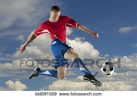 Stock Photo - Caucasian soccer player jumping in mid-air kicking ball. Fotosearch