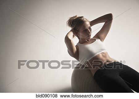 Stock Photo - Caucasian woman doing sit-ups on exercise ball. Fotosearch