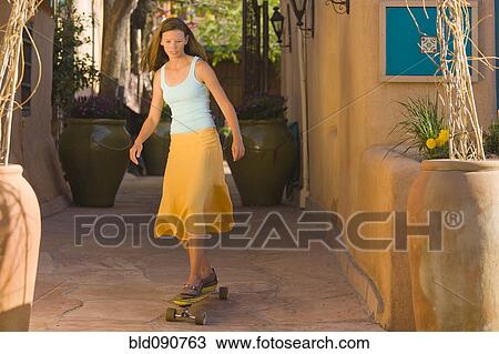 Stock Image - Caucasian woman skateboarding on sidewalk. Fotosearch
