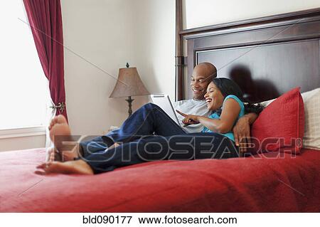 Couple laying on bed using digital tablet together View Large Photo Image Stock Photo - Couple laying on bed using digital tablet together. Fotosearch