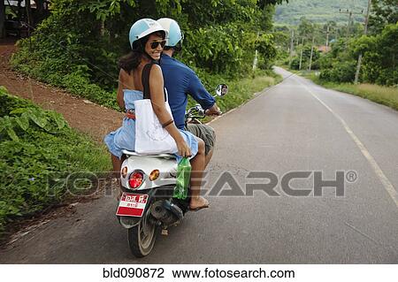 Stock Image - Couple riding scooter in remote area. Fotosearch