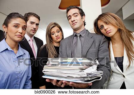 Stock Photograph - Frustrated Hispanic business people with pile of paperwork. Fotosearch