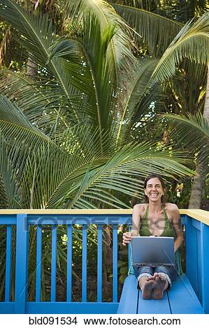 Picture - Grinning Hispanic woman using laptop on deck. Fotosearch