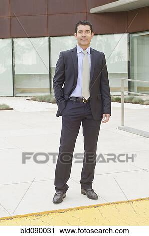 Stock Image - Hispanic businessman standing in office courtyard. Fotosearch
