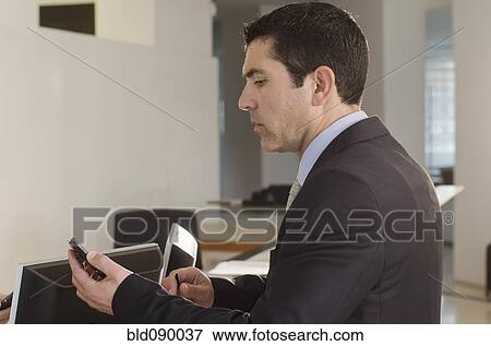 Stock Photo - Hispanic businessman text messaging on cell phone in office. Fotosearch