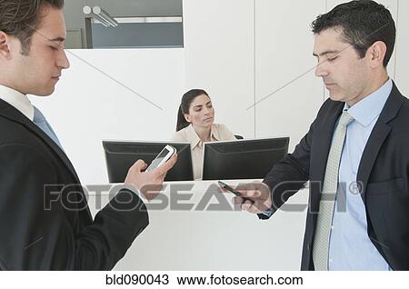 Stock Image - Hispanic businessmen holding cell phones in office. Fotosearch