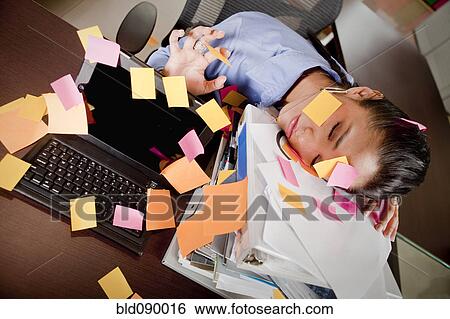 Stock Photograph - Hispanic businesswoman covered in sticky notes sleeping at desk. Fotosearch