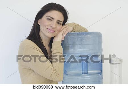 Stock Photo - Hispanic businesswoman leaning on water cooler. Fotosearch
