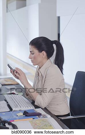 Stock Photograph - Hispanic businesswoman text messaging at desk. Fotosearch