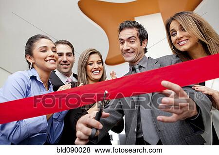 Stock Photo - Hispanic co-workers watching businessman cutting red ribbon. Fotosearch