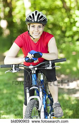 Stock Image - Hispanic woman riding mountain bike in forest. Fotosearch