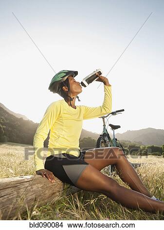 Picture - Mixed race biker taking a break and drinking water. Fotosearch