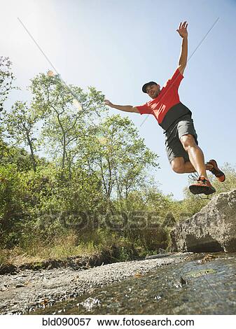 Stock Photo - Mixed race man jumping into stream. Fotosearch