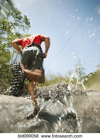 Stock Photo - Mixed race man running through stream. Fotosearch