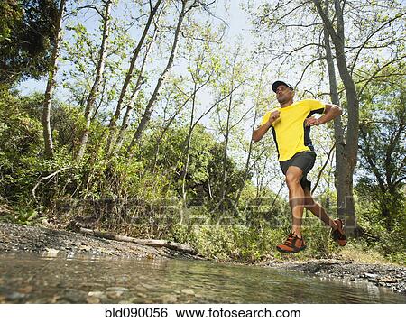 Stock Photograph - Mixed race man running through stream. Fotosearch