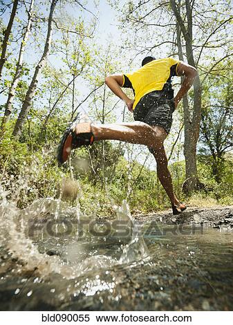 Stock Photography - Mixed race man running through stream. Fotosearch