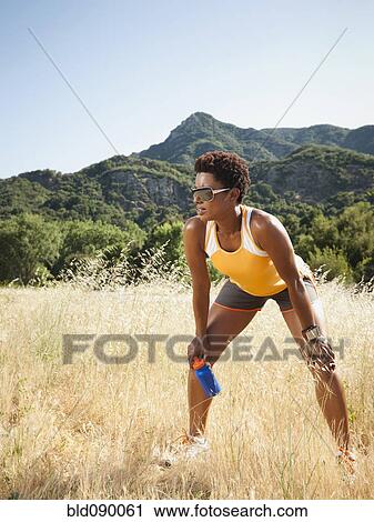 Stock Image - Mixed race runner relaxing in remote field. Fotosearch