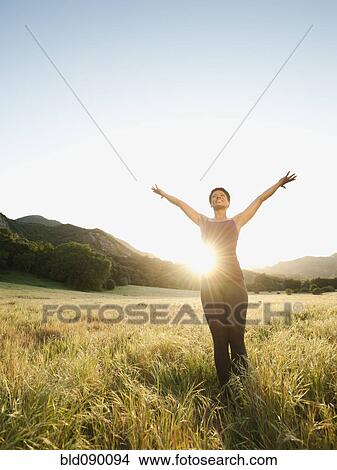 Picture - Mixed race standing in remote field with arms outstretched. Fotosearch
