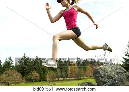 Stock Image - Mixed race teenager jumping from rock. Fotosearch