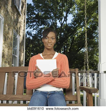 Stock Image - Mixed race woman holding paperwork on porch. Fotosearch