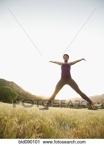 Stock Image - Mixed race woman jumping in remote field. Fotosearch