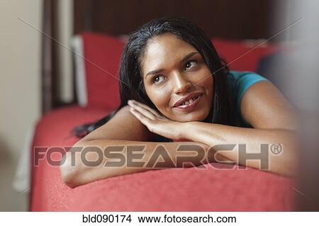 Picture - Mixed race woman laying on bed daydreaming. Fotosearch