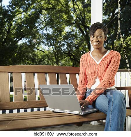 Stock Photo - Mixed race woman on porch using laptop. Fotosearch