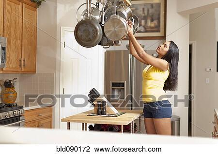 Stock Image - Mixed race woman reaching for pan in kitchen. Fotosearch