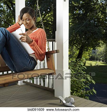 Stock Photo - Mixed race woman reading on porch. Fotosearch