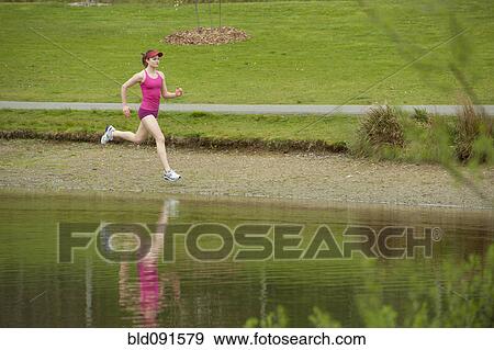 Stock Photo - Mixed race woman running near pond. Fotosearch