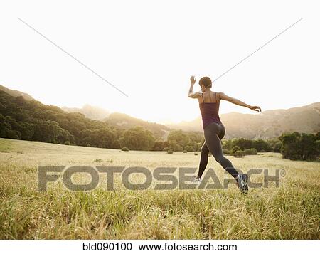 Stock Image - Mixed race woman running through remote field. Fotosearch