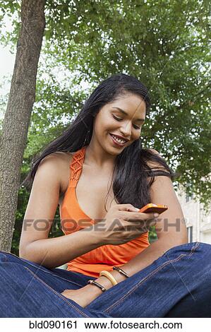 Stock Image - Mixed race woman text messaging on cell phone outdoors. Fotosearch