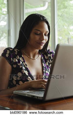 Stock Photograph - Mixed race woman typing on laptop. Fotosearch