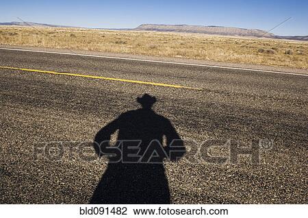Stock Image - Shadow of cowboy on remote highway. Fotosearch