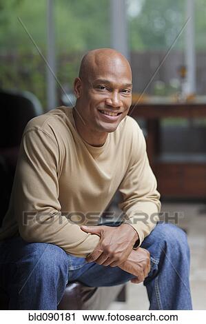 Stock Image - Smiling Black man sitting in chair. Fotosearch