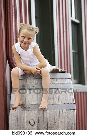 Stock Image - Smiling Caucasian girl sitting on barrel. Fotosearch