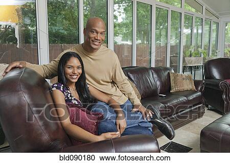 Smiling couple sitting in living room together View Large Photo Image Stock Image - Smiling couple sitting in living room together. Fotosearch