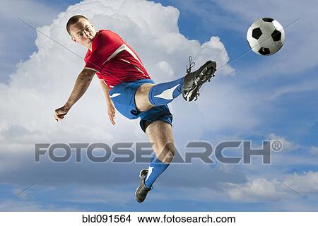 Picture - Soccer player jumping in mid-air kicking ball. Fotosearch