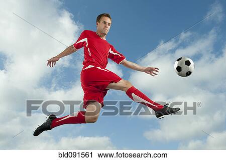 Stock Image - Soccer player jumping in mid-air kicking ball. Fotosearch