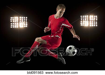 Soccer player jumping in mid-air kicking ball at night View Large Photo Image Stock Image - Soccer player jumping in mid-air kicking ball at night. Fotosearch