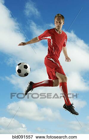Stock Photo - Soccer player jumping in mid-air kicking ball. Fotosearch